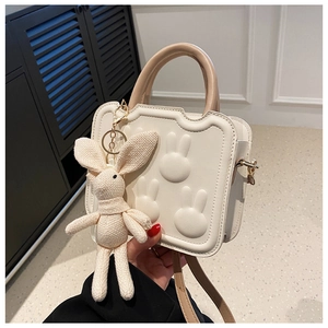 Close-up of creamy white crossbody bag with embossed rabbit heads and knit bunny charm