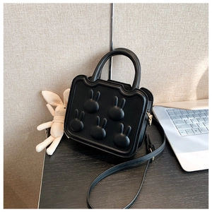 Close-up of black leather bag with embossed rabbit heads on a wooden desk with a plush toy