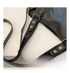 Detail view of the black leather tote bag showing silver metal ring and rivet strap attachment