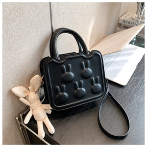 Detail of black square handbag featuring rabbit embossed patterns and a plush charm