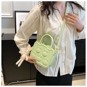 Close-up of light green crossbody bag with rabbit embossments and knit pendant charm