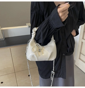 Détail du sac à main blanc plissé avec nœud en perles et pendentif en forme de cœur