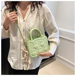 Close-up of a light green crossbody bag with rabbit embossment and plush charm