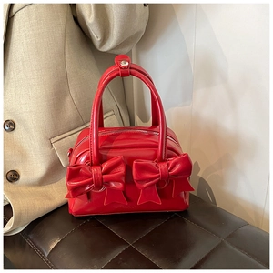 Detail of red bow pillow bag on dark leather bench with textured leather finish