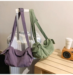 Canvas messenger bags in purple and army green hanging on white suitcase handle