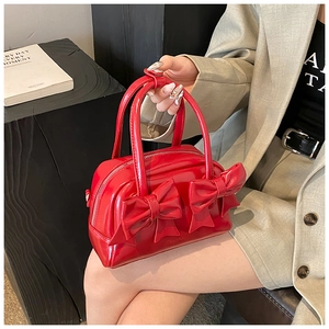 Detail of red glossy leather handbag featuring two large decorative bows and dual handles