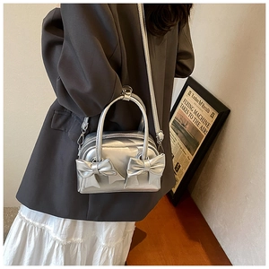 Detail view of silver bow handbag with metallic texture and embossed MUDU logo detail