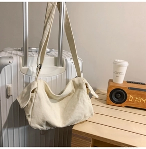 Minimalist beige canvas crossbody crescent bag hanging on suitcase with coffee cup
