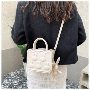 Detail of cream square crossbody bag with embossed rabbit and plush charm on a model