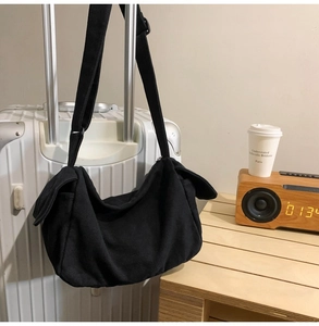 Detail of black canvas crossbody bag with decorative flaps hanging on a white suitcase