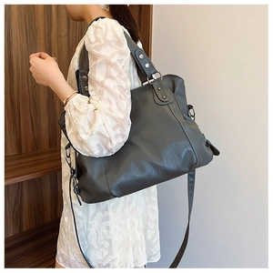 Dark grey leather tote bag shown on shoulder with silver rivets and metal ring details