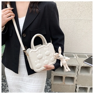Close-up of creamy white crossbody bag featuring 3D rabbit embossing and knit pendant