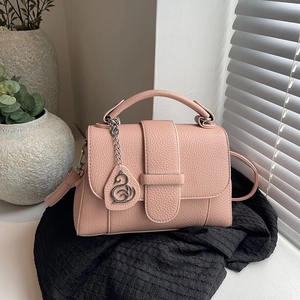 Pink lychee grain leather handbag with swan charm on a minimalist textured background