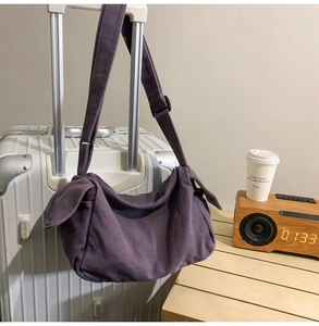 Detail view of purple canvas crossbody bag hanging on a suitcase with adjustable strap
