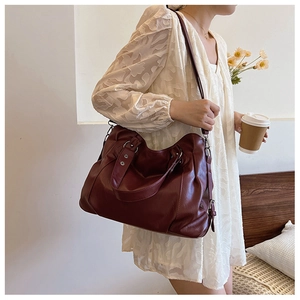 Detail view of large burgundy leather tote bag styled on a female model with a shoulder strap