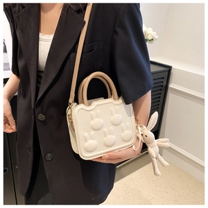 Close-up of a white square crossbody bag featuring 3D rabbit embossing and a plush charm