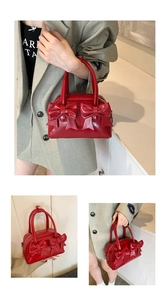 Detail of red glossy bow handbag with dual handles and structured Boston style design