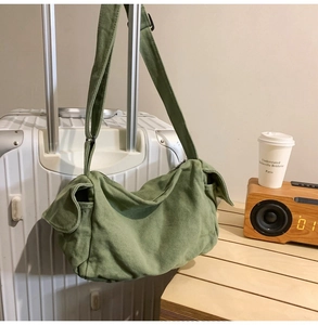 Detail of dark green canvas crossbody bag hung on suitcase handle in a cozy setting