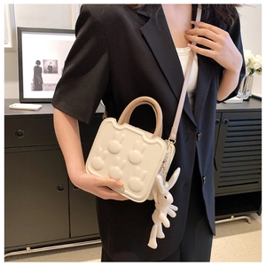 Close-up of a white wave-shaped handbag with 3D rabbit relief and a plush bunny charm