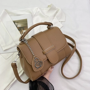 Brown lychee leather handbag with metal buckle and swan pendant on a white suit background