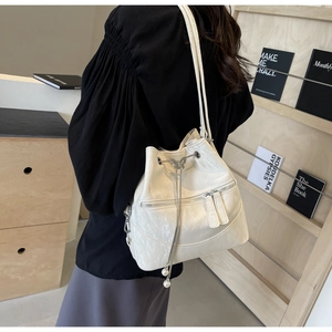 Detail der cremeweißen Leder-Beuteltasche mit Schmetterlings-Kordelzug und Reißverschlusstaschen