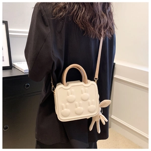 Detail view of cream mini handbag with rabbit reliefs and plush charm worn by model
