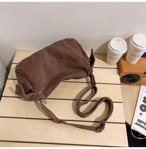 Close-up of a large brown canvas crossbody bag on a wooden table with lifestyle props