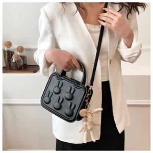 Detail of black crossbody bag with rabbit motifs and plush bunny charm on white blazer