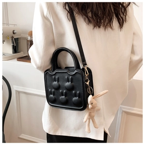 Detail of black crossbody bag with rabbit relief motifs and knitted bunny pendant charm