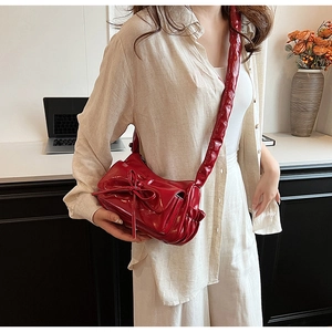 Detail of red patent leather crossbody bag with a large bow and pleated shoulder strap