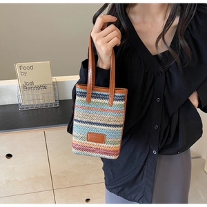 Detail of colorful striped woven bucket bag with brown leather handles and brand patch