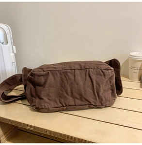 Detail view of a vintage dark brown canvas crossbody bag resting on a wooden table