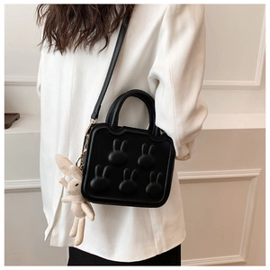 Detail of black crossbody bag with 3D rabbit patterns and a white woven doll pendant