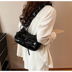 Detail of black glossy PU leather shoulder bag with pleated strap and bow knot design