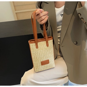Détail du petit sac seau en paille avec poignées en cuir marron et étiquette