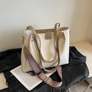 Grand cabas en cuir beige avec anses brunes et large bandoulière sur veste en cuir noir