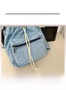 Close-up of light blue denim bucket bag showing drawstring closure and front zipper pocket