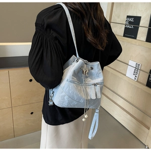 Detail eines hellblauen Plissee-Rucksacks mit Metall-Schmetterling und Perlen-Anhänger
