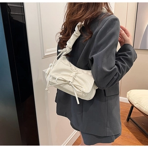 Detail of creamy white pleated crossbody bag featuring a large bow and ruffled shoulder strap
