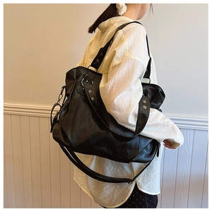 Detail of black faux leather tote bag with silver rivets and multi-strap design on model