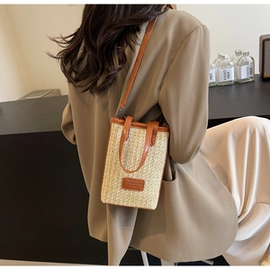 Détail du sac seau en paille avec garniture en cuir brun porté avec un blazer beige