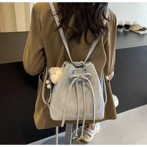 Detail eines hellblauen Eimer-Rucksacks mit Kordelzug, Marmortextur und Bärchenanhänger