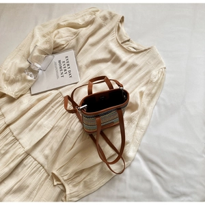 Vue à plat du sac seau en paille tissée colorée avec bandoulière en cuir et robe beige