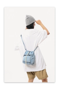 Rear view of model wearing a light blue denim drawstring bucket bag with casual crossbody strap