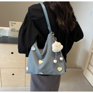 Detail of blue tote bag with heart patches, plush cloud charm, and metal chain strap