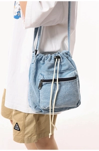Close-up of light blue denim bucket bag with drawstring closure and zip pocket