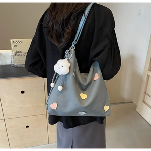 Detail of grey-blue canvas hobo bag with colorful heart patches and cloud charm