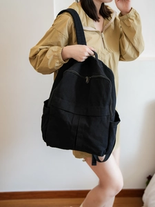 Détail du grand sac à dos en toile noire porté par un mannequin dans un studio clair