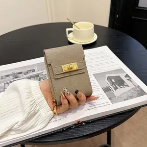 Minimalist taupe leather card holder with gold turn-lock closure on wooden table