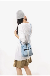 Detail of light blue denim drawstring bucket bag with black zipper pocket and cotton ropes
